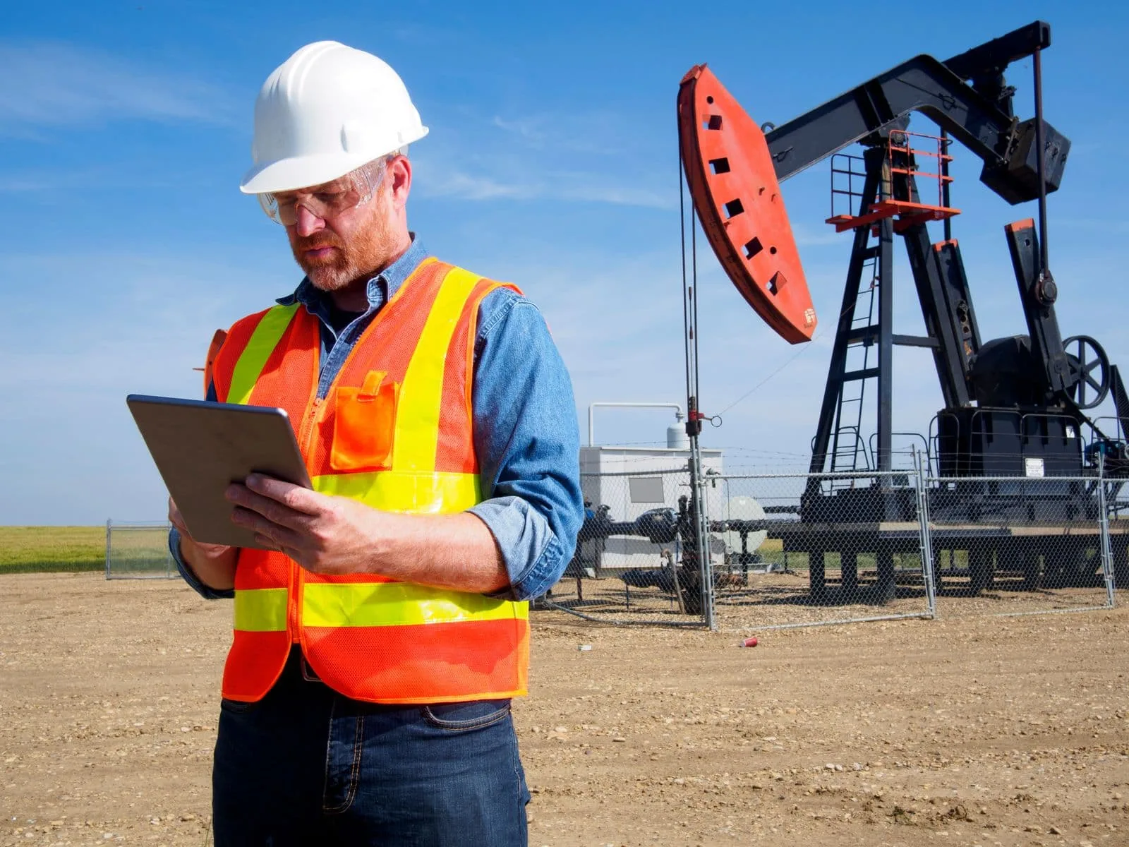An inspector with a tablet beside an oil pumpjack