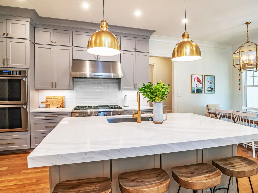 A bright remodeled kitchen with a marble island, brass pendant lights and wood stools